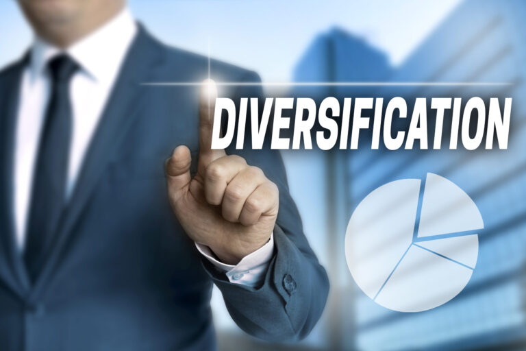 A man in a suit touches a virtual screen displaying the word DIVERSIFICATION with a glowing effect—a business imperative. A pie chart is visible in the lower right corner, while a blurred cityscape provides the backdrop.