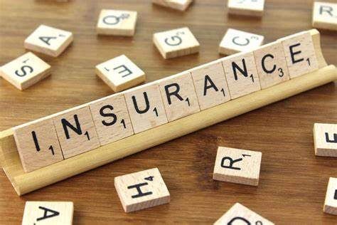 Scrabble tiles spell INSURANCE on a wooden rack, surrounded by scattered letter tiles on a wooden surface, symbolizing managing risk in everyday life.