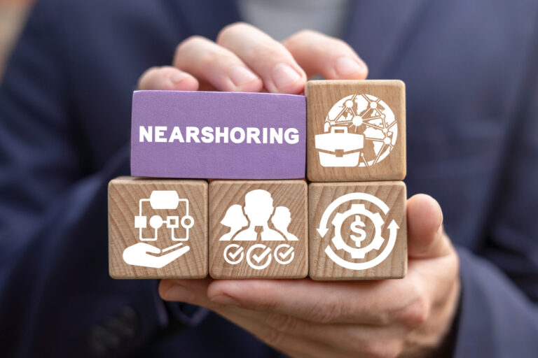 A person displays wooden blocks illustrating Nearshoring, adorned with icons like a robotic hand and a globe with gears. In the background, amid the blurred silhouette of a dark suit, lies South Americas emerging hub for software developers in 2024.