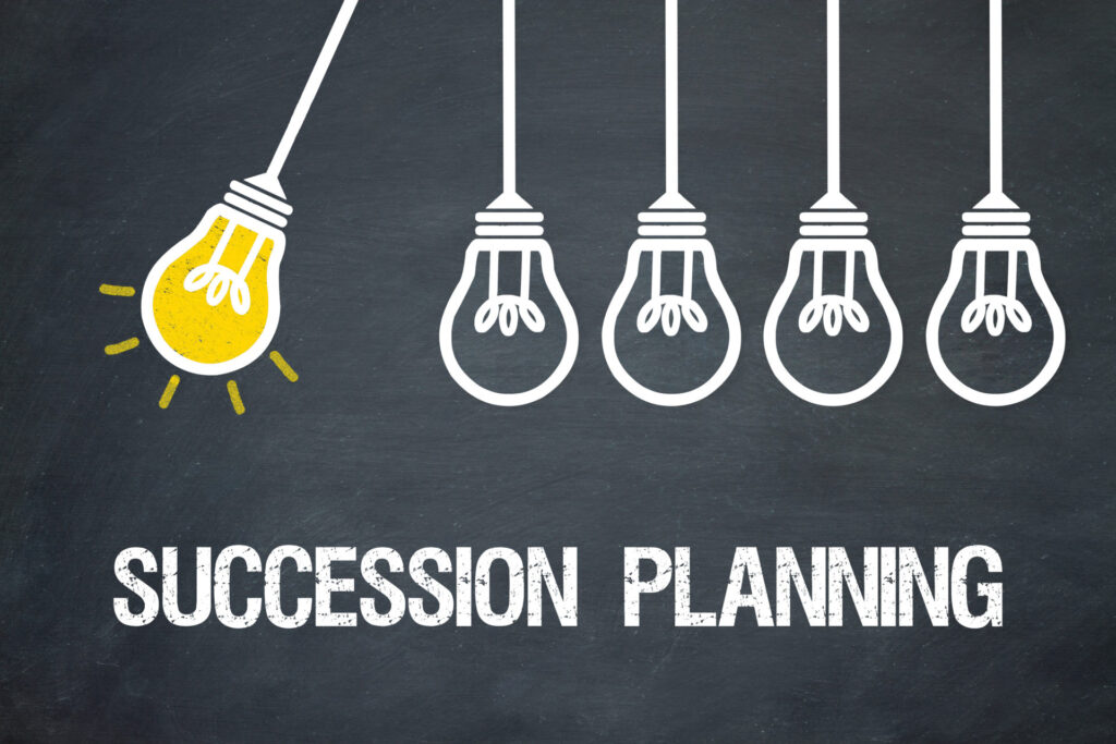 Illustration of five hanging light bulbs against a chalkboard background. The leftmost bulb is lit, symbolizing a bright idea or leadership. Text below reads Recruiting and Succession Planning in white chalk-like font.